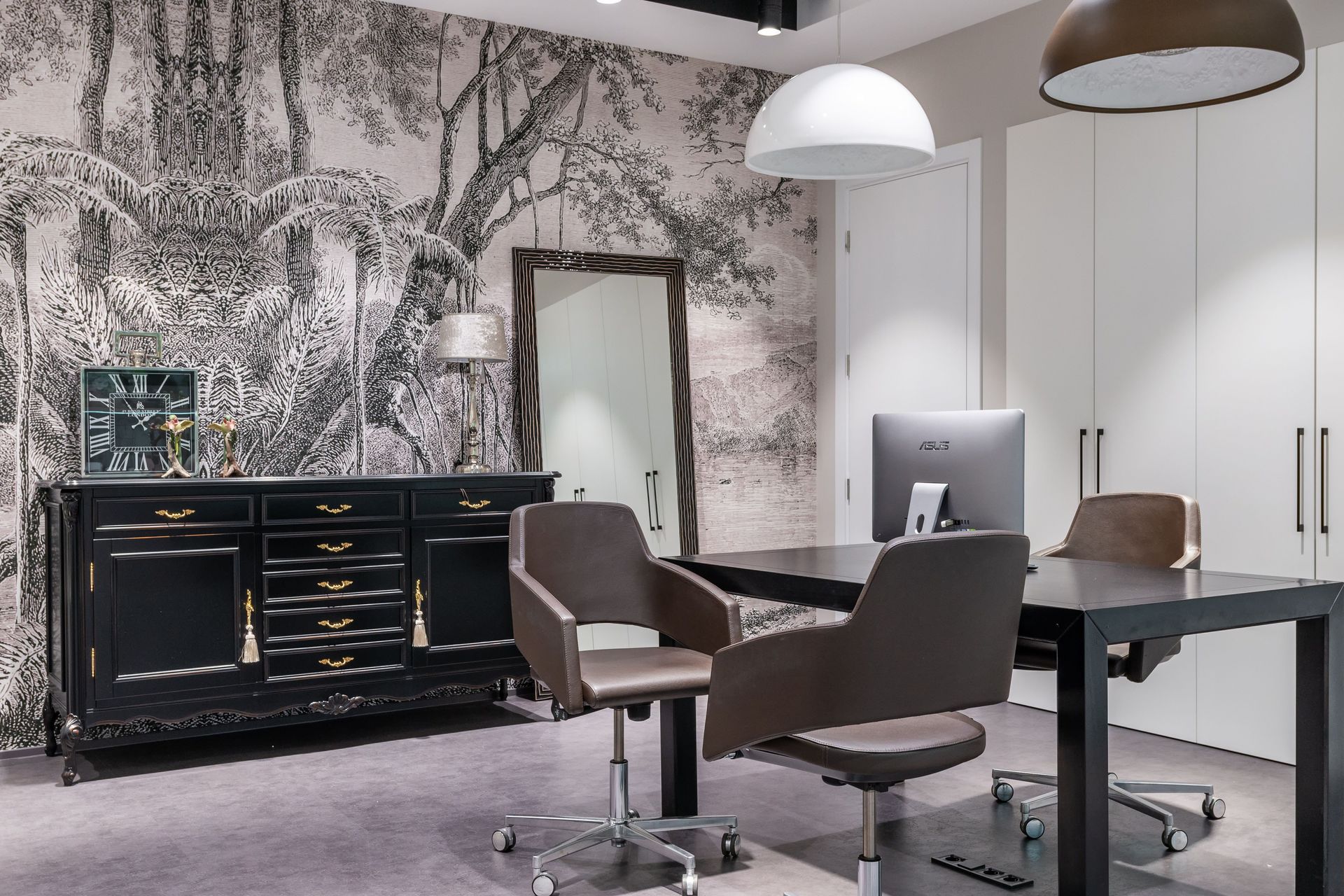 Modern computer on black table near armchairs placed in living room near cabinet with clock in spacious apartment with mirror and closet